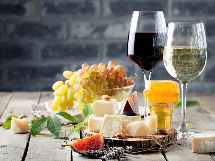 Grape, cheese, figs and honey with a glasses of red and white wine on a stone and wood background